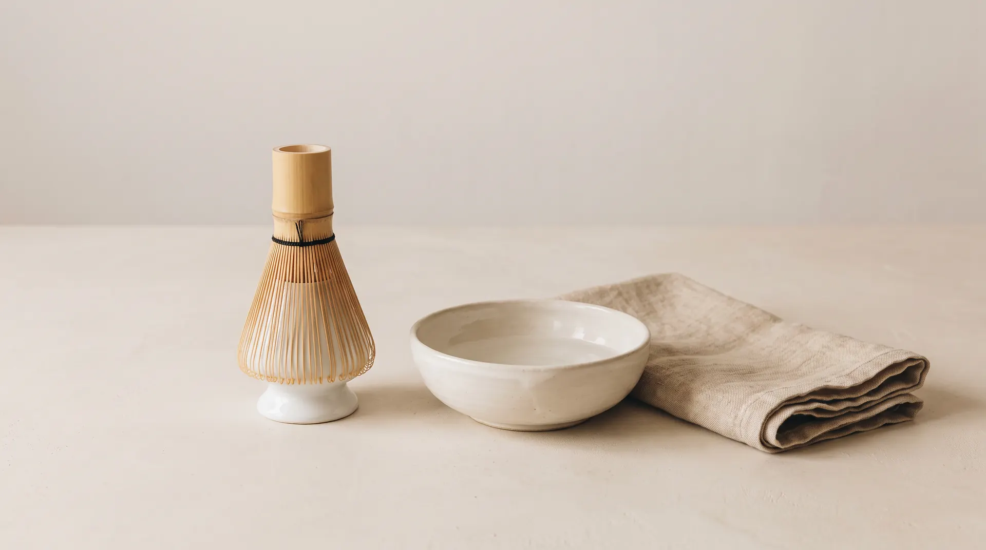 Bambusowa miotełka chasen susząca się na ceramicznym stojaku kusenaoshi, obok miseczka z wodą i złożona lniana ściereczka.